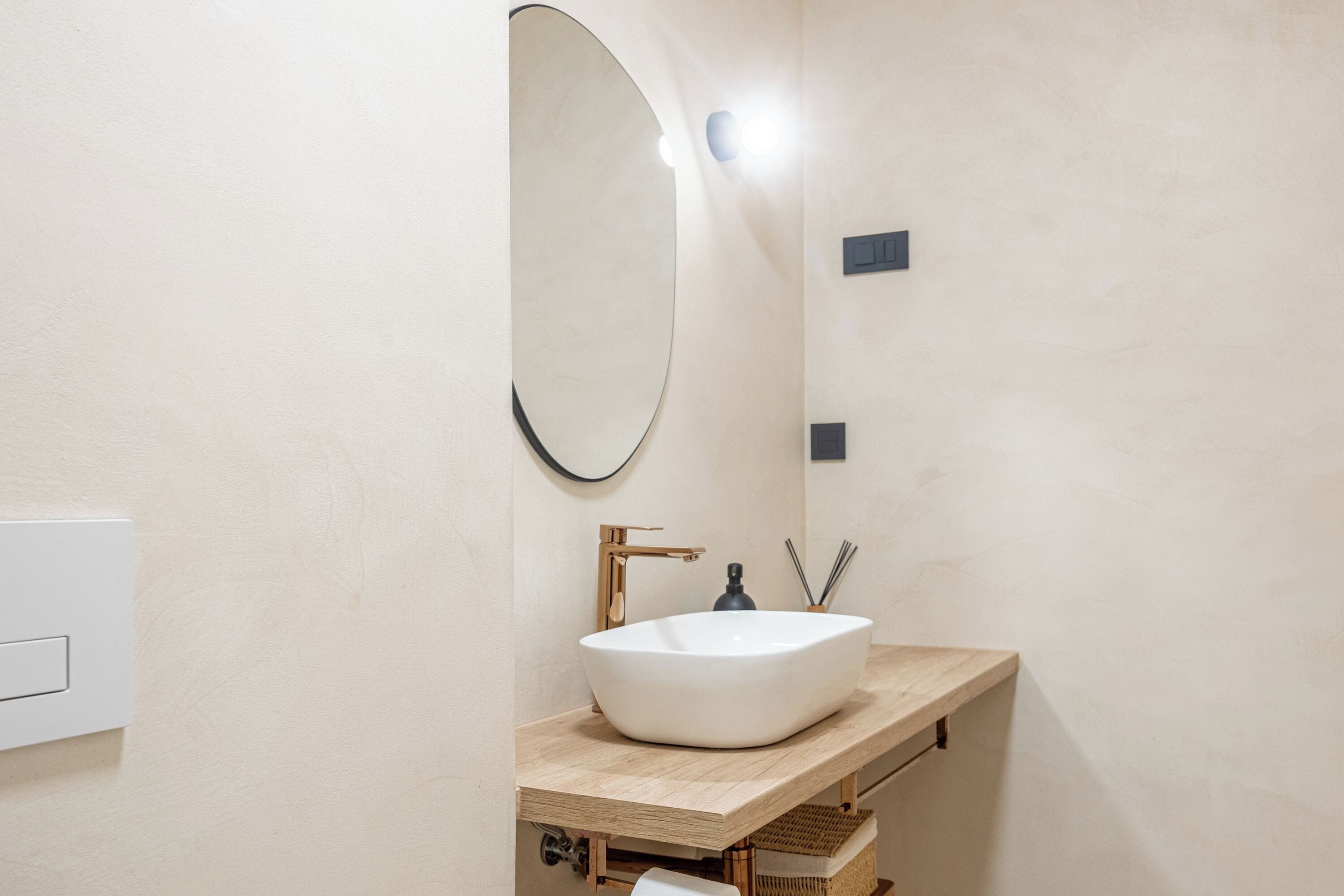A bathroom with a white sink, a round mirror, and a wooden countertop.
