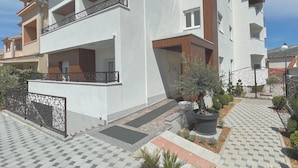 A modern multi-story residential building with balconies, a paved driveway, and a landscaped garden area.