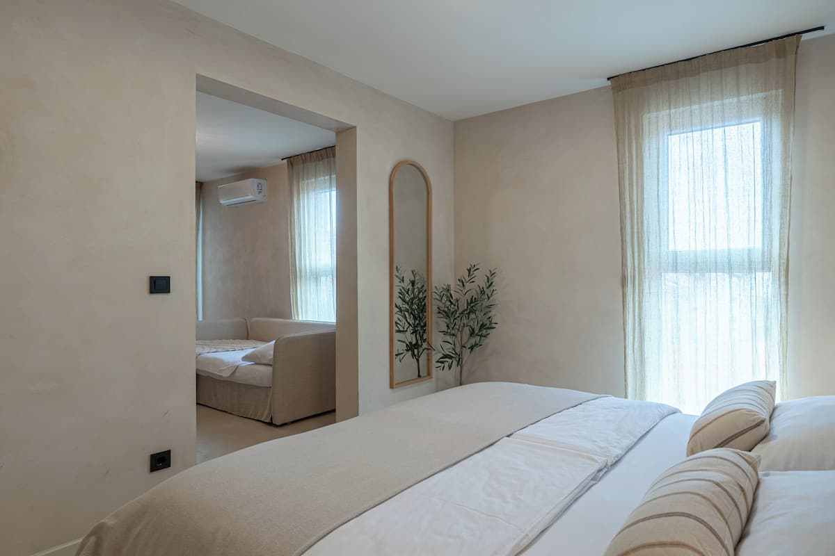 A bedroom with a large bed, a mirror, and a window with curtains.