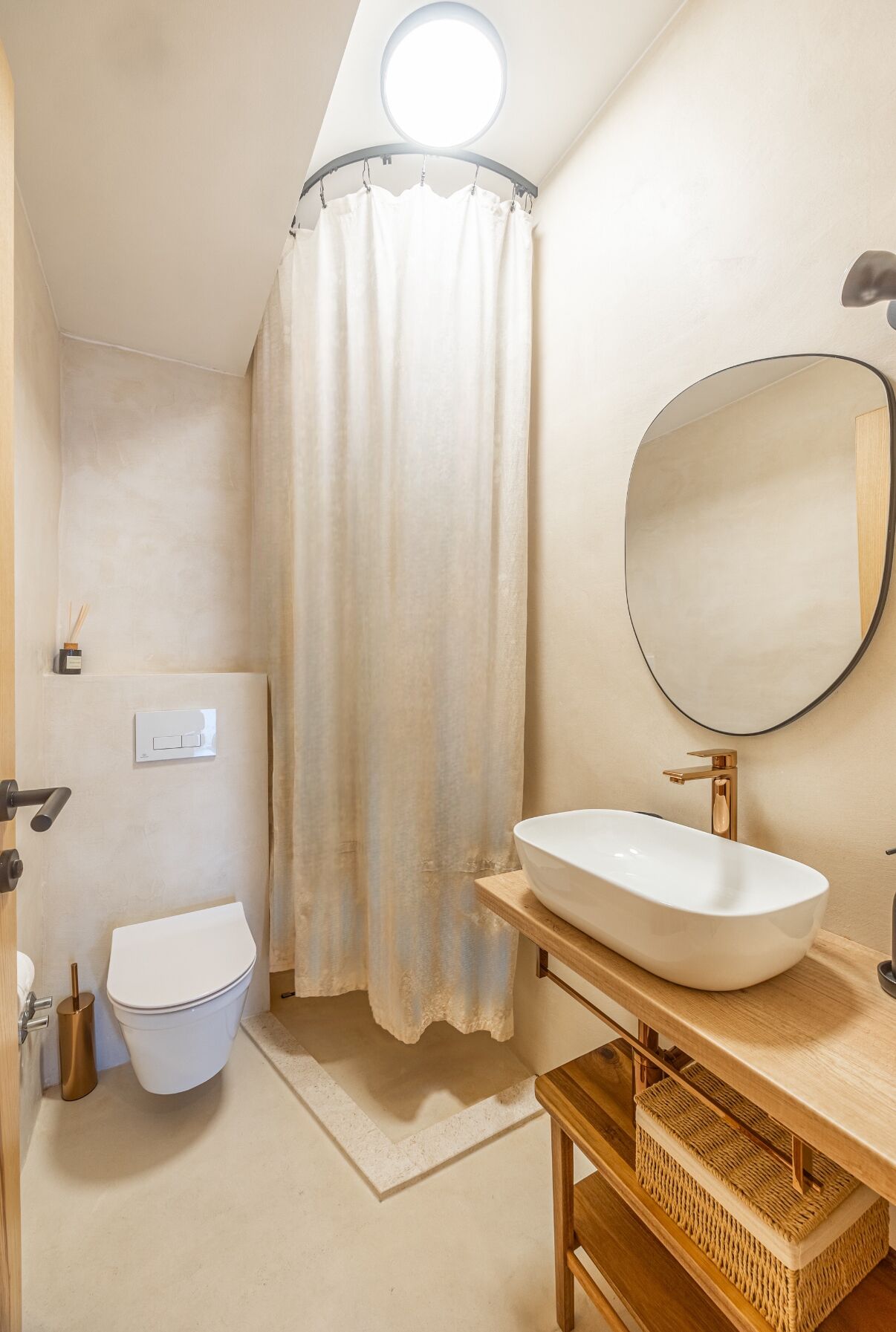 Un baño con inodoro blanco, espejo redondo y lavamanos con grifo dorado.