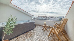 A rooftop terrace with a hot tub, wooden chairs, and a potted plant.