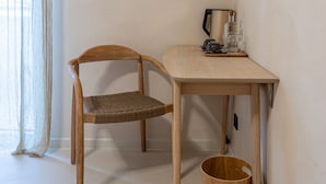 A small, simple room with a wooden chair, a table, a kettle, and a TV mounted on the wall.