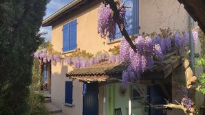 A house with purple wisteria hanging over the entrance, a tiled roof, and a small porch with a chair. - Maison, Piscine Privée et Terrain de Boules, au Calme (Trévoux)