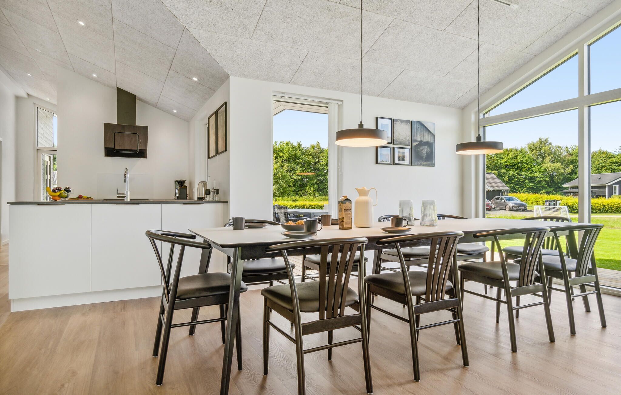 Une cuisine moderne dotée d’un grand îlot central, d’un coin repas avec des chaises et de grandes fenêtres offrant une vue sur l’extérieur.