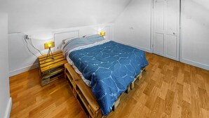 A bedroom with a bed on wooden pallets, two bedside lamps, and a wardrobe. - 1 bedroom lovely home in Lannéanou (Lannéanou)