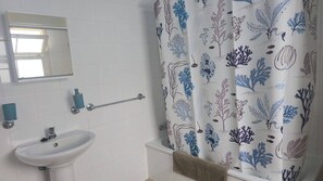 Un bagno con un lavandino bianco, un porta asciugamani e una tenda da doccia con un motivo floreale blu e viola.
