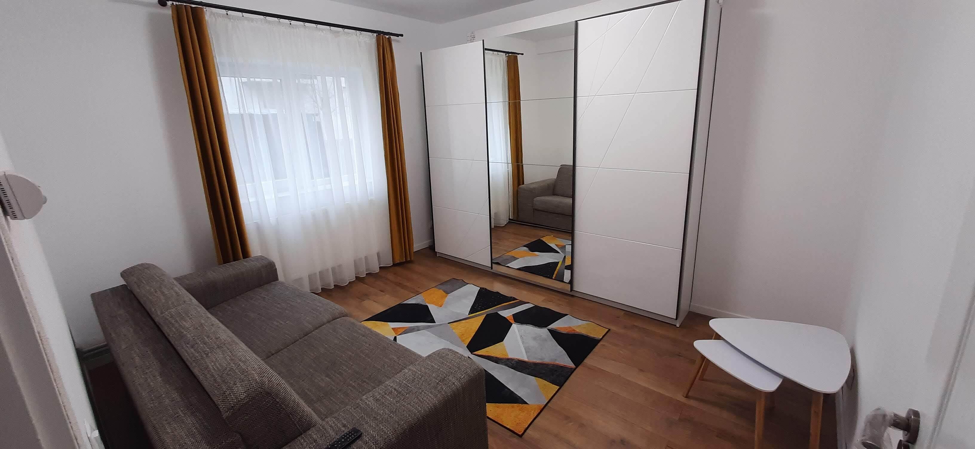 Una sala moderna con un sofá, una mesita, un tapete estampado y un espejo integrado en una puerta corredera.