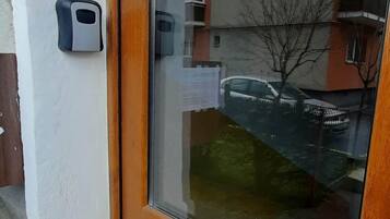 Una puerta de madera con un panel de vidrio, un timbre y el reflejo de un edificio con balcones.