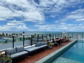 Un espace piscine sur le toit avec vue sur l’océan, des sièges extérieurs et un coin repas.