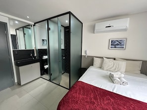 A hotel room with a bed, a red throw, a wall-mounted air conditioner, a telephone, and a framed picture. - Bela Hospedagem - Get One Bessa (João Pessoa)