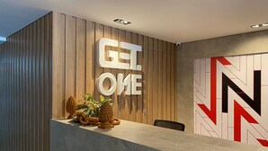Een receptiebalie met een houten paneelwand, een groot 'GET ONE' bord en een abstract kunstwerk aan de muur.