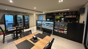 Een café met een toonbank vol snacks en dranken, een zithoek met tafels en stoelen, en automaten.