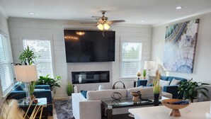 A modern living room with a flat-screen TV, a ceiling fan, and a dining area with a wooden table and chairs. - Boating, Fishing, Kayaking and more at this NEW Waterfront Bay St. Louis Retreat (Bay St. Louis)