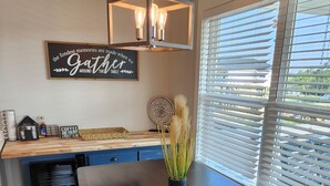 A dining area with a large wooden table, benches, a hanging light fixture, a decorative sign, and a window with blinds. - Boating, Fishing, Kayaking and more at this NEW Waterfront Bay St. Louis Retreat (Bay St. Louis)