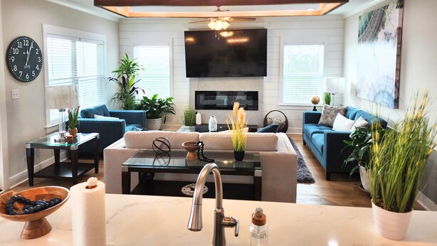 A modern living room with a flat-screen TV, two sofas, a coffee table, and a kitchen area with a sink and countertop. - Boating, Fishing, Kayaking and more at this NEW Waterfront Bay St. Louis Retreat (Bay St. Louis)