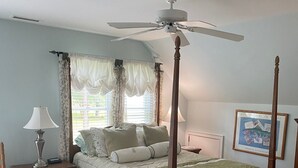 Une chambre à coucher avec un lit à baldaquin, un ventilateur de plafond, une table de chevet avec une lampe et un tableau encadré au mur.