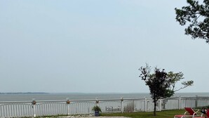 Une piscine avec vue sur la mer, entourée d’une clôture blanche et d’un arbre.
