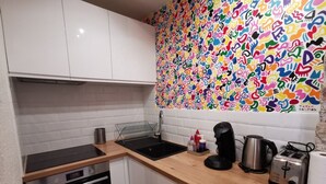 Una cocina con armarios blancos, horno de acero inoxidable, lavavajillas, fregadero, cafetera, tostadora y un llamativo mural abstracto en la pared.