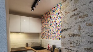 Cocina compacta con armarios blancos, lavadora, tostadora y un llamativo mural abstracto.