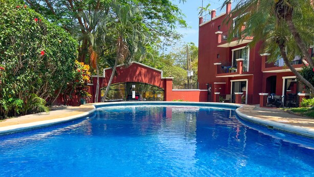 A clear blue pool with a red building in the background. - 2BR/2BR w/Rooftop Terrace, steps from the Beach, Tamarindo Condo (Tamarindo)
