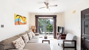 A living room with a sofa, a chair, a television, and a ceiling fan. - 2BR/2BR w/Rooftop Terrace, steps from the Beach, Tamarindo Condo (Tamarindo)