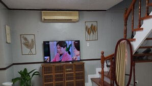 Un salon avec une télévision, un meuble en bois, un escalier et des plantes en pot.