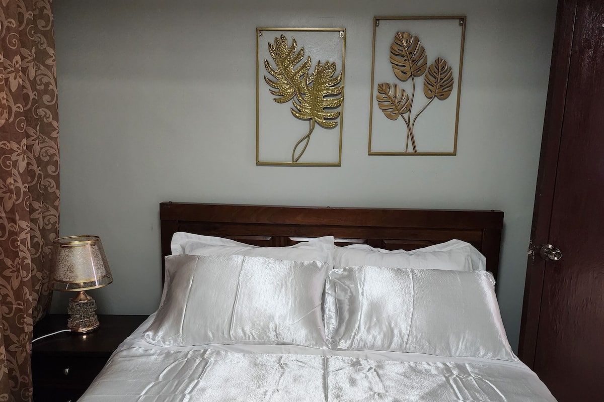 Una cama bien hecha con sábanas blancas, un cabecero de madera y dos adornos de hojas enmarcados en la pared.