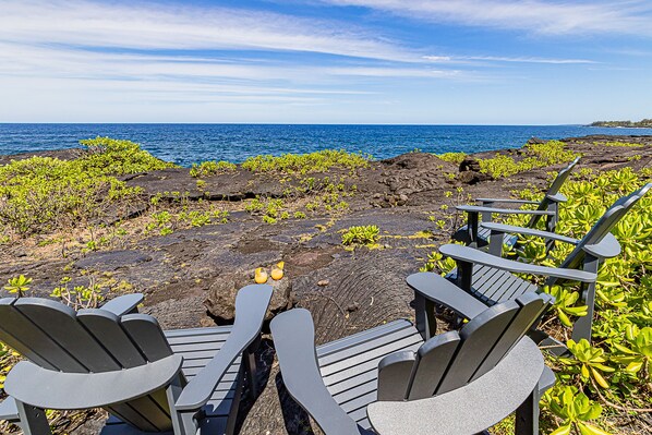 A seating area with Adirondack chairs overlooking a rocky coastline and the ocean. - Pele's Paradise- Absolute Oceanfront Paradise with Air Conditioning! (Keaau)