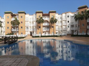 Relax by the pool surrounded by lush palm trees and a wooden bridge.