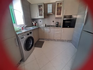 Compact kitchen with a washing machine, coffee maker, and microwave, offering a functional space for cooking and laundry.