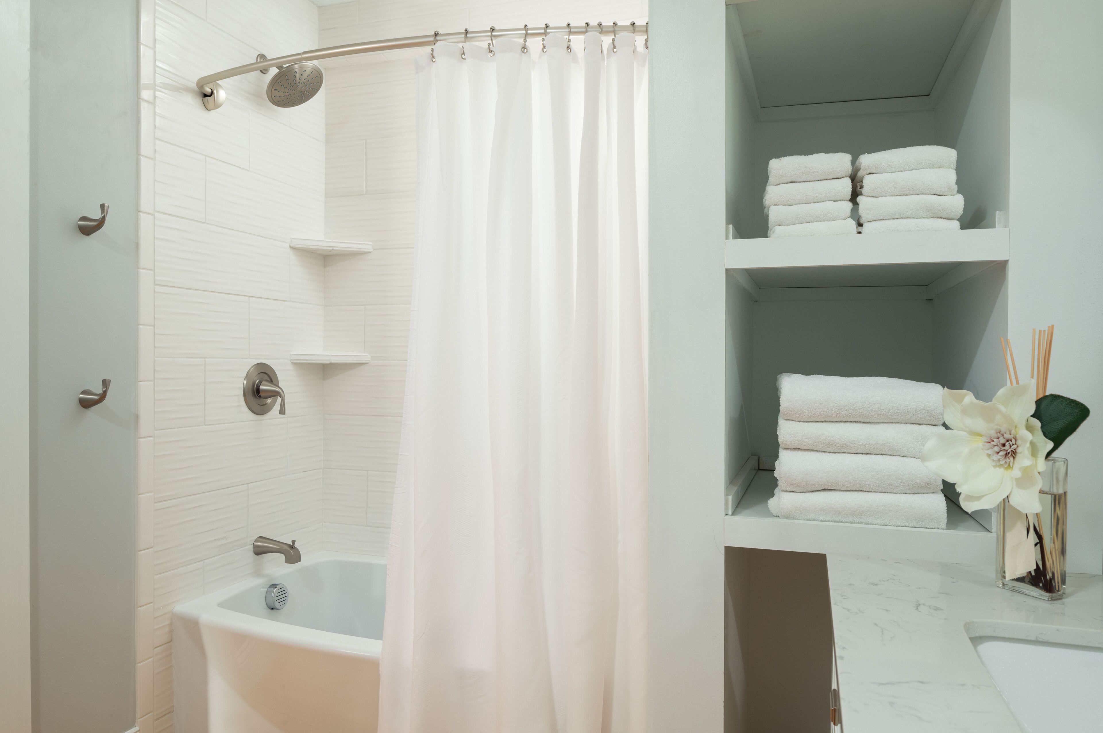 A modern bathroom with a bathtub, shower curtain, and neatly stacked towels on shelves.