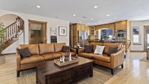 Un salón amplio con un sofá de cuero marrón, una mesa de centro de madera y una cocina con armarios de madera y electrodomésticos de acero inoxidable.