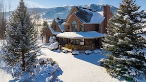 Una casa grande de dos pisos con techo nevado y un porche cubierto.