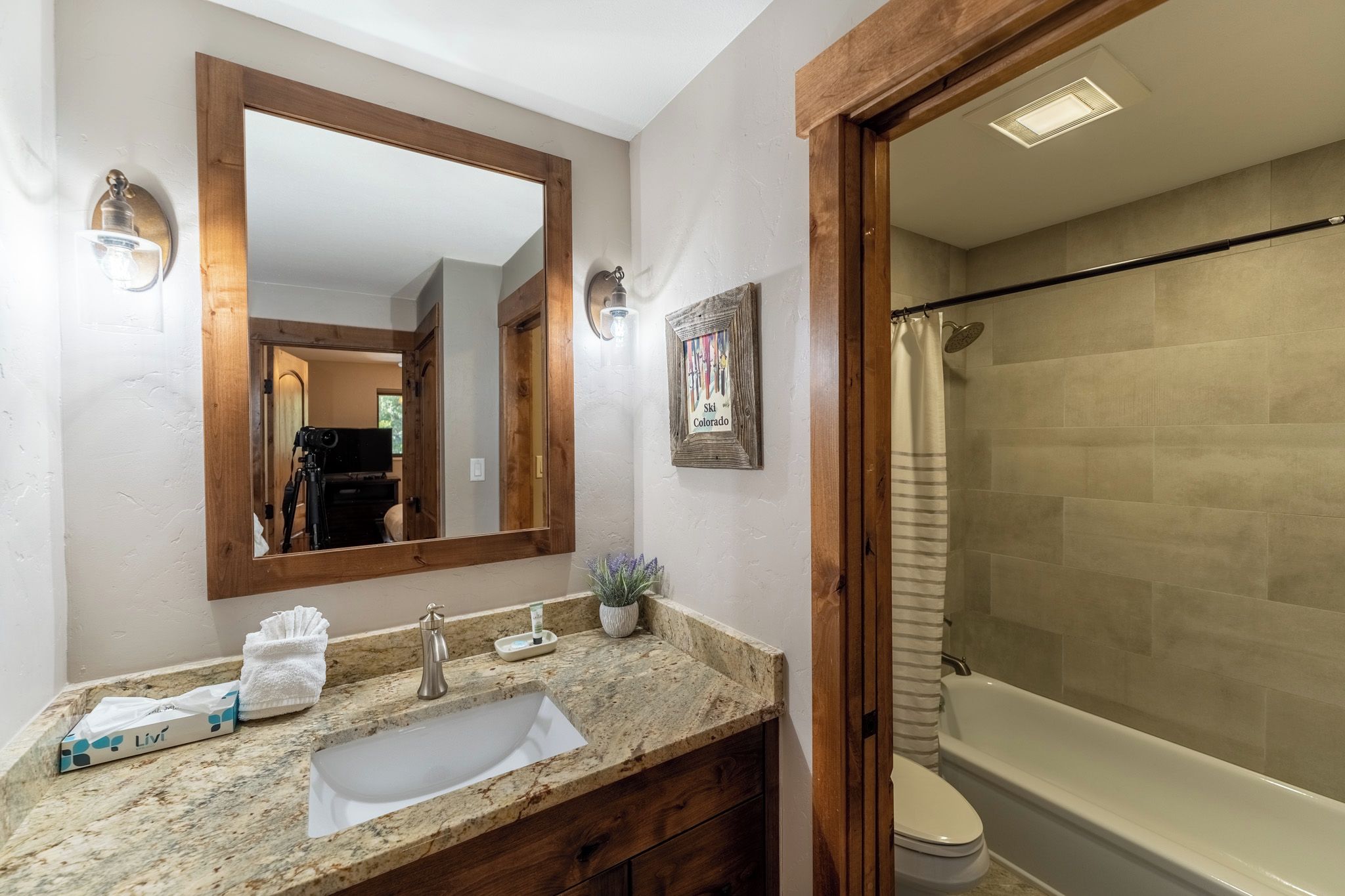 A bathroom with a granite countertop, a sink, a mirror, a shower area, and a framed picture on the wall.