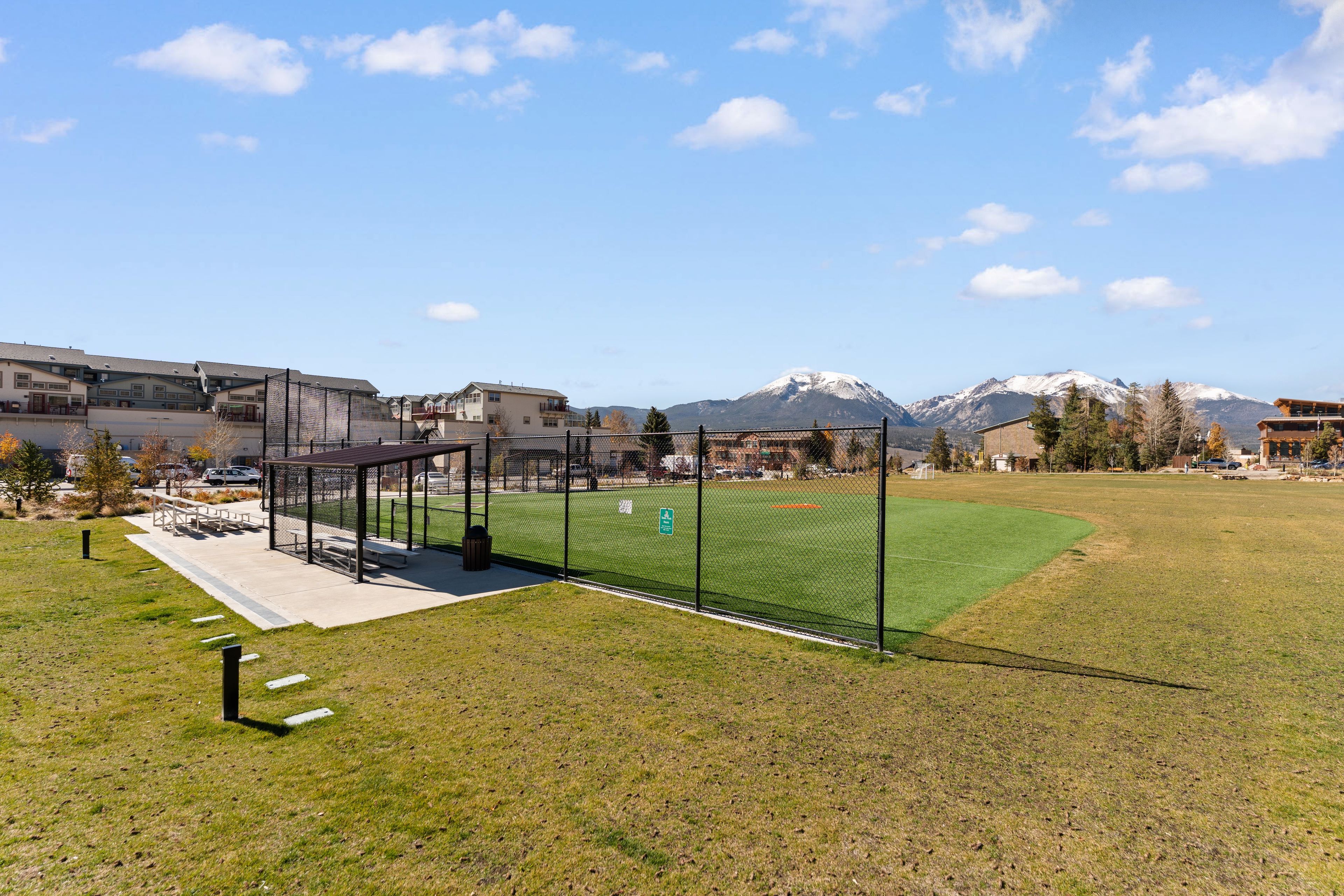 A sports field with a fence, a covered seating area, and buildings in the background.