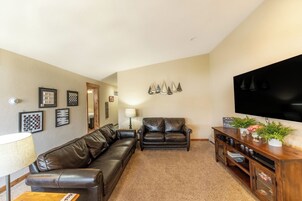 A living room with a brown leather sofa, a wooden entertainment unit with plants, and a flat-screen TV mounted on the wall.