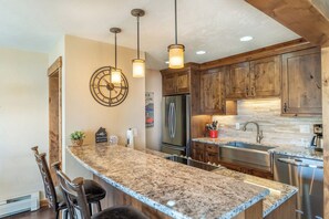 A kitchen with granite countertops, wooden cabinets, stainless steel appliances, pendant lighting, and a clock on the wall. - Lake Cliffe #303, Building E By Summit County Mountain Retreats (Dillon)
