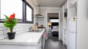 Et moderne køkken med en central ø, en sort gryde med røde blomster, og udsigt til et soveværelse med seng og natbord.