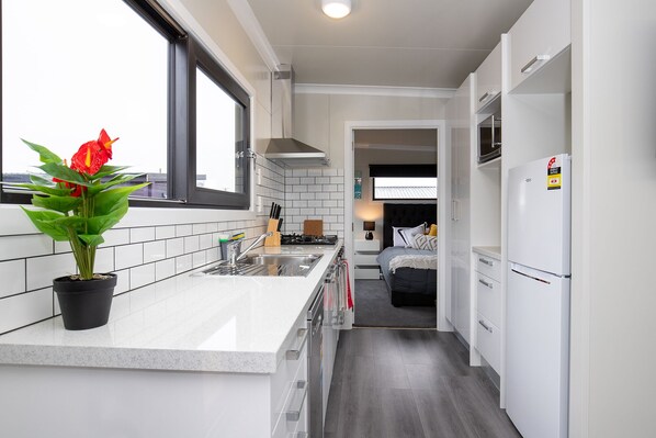 Une cuisine moderne avec un îlot central, un pot noir orné de fleurs rouges et une vue sur une chambre à coucher avec un lit et une table de chevet.