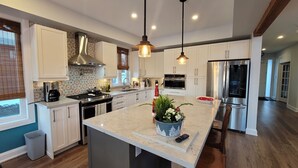 Una cocina moderna con armarios blancos, electrodomésticos de acero inoxidable, una isla de mármol e iluminación colgante.