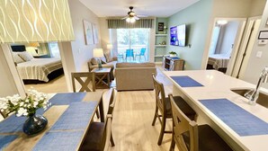 A modern kitchen with a central island, dining area with chairs, and a living room with a sofa and chairs.