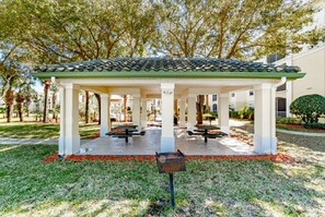 A covered outdoor seating area with tables and benches, surrounded by trees and a building in the background. - 2-104 Legacy Dunes Resort, Ground Floor Lake View, Heated Pool,Gym (Kissimmee)