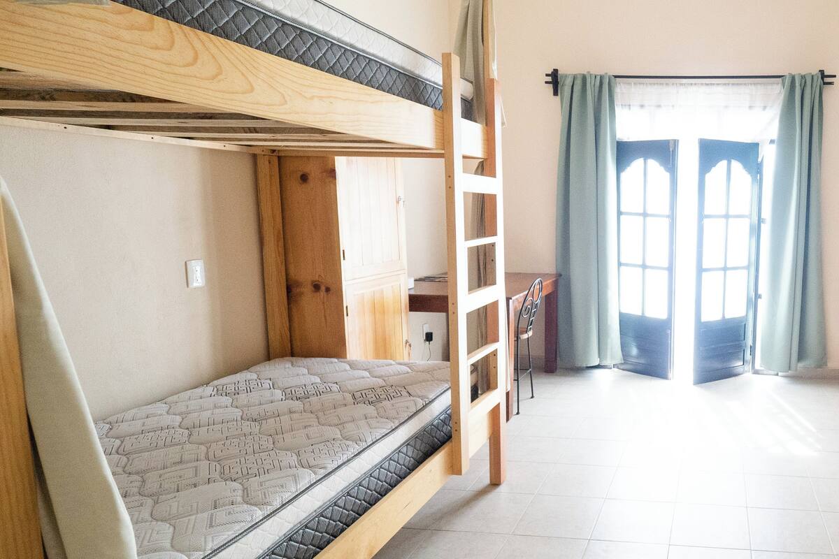 A bunk bed room with a wooden ladder, a small desk, and a window with curtains.