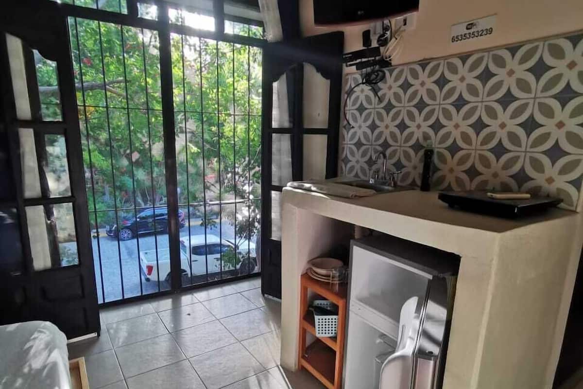A compact kitchen with a refrigerator, a sink, and a small countertop. There is a TV mounted on the wall above the countertop.