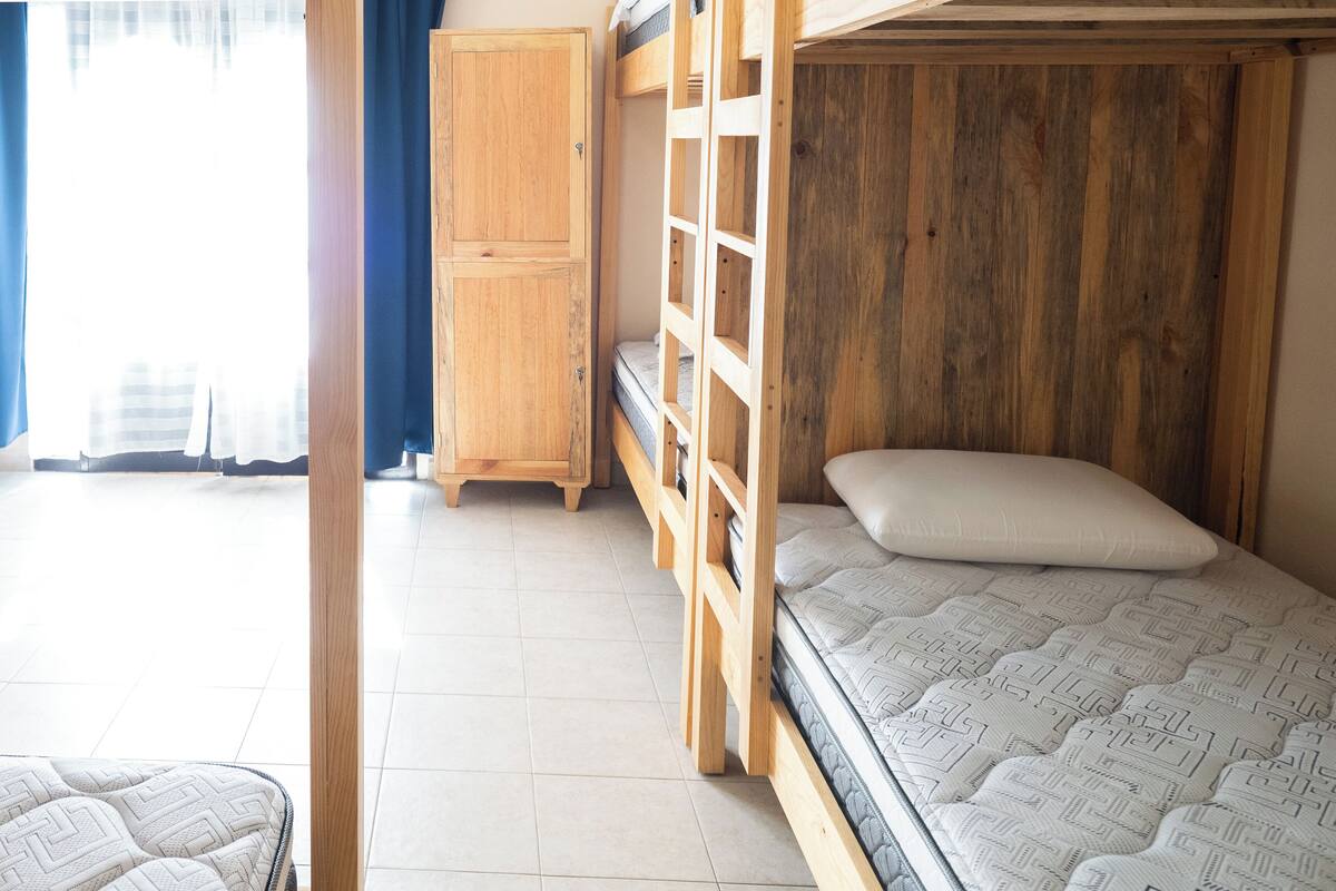 A dormitory room with bunk beds, a wooden wardrobe, and a window with curtains.