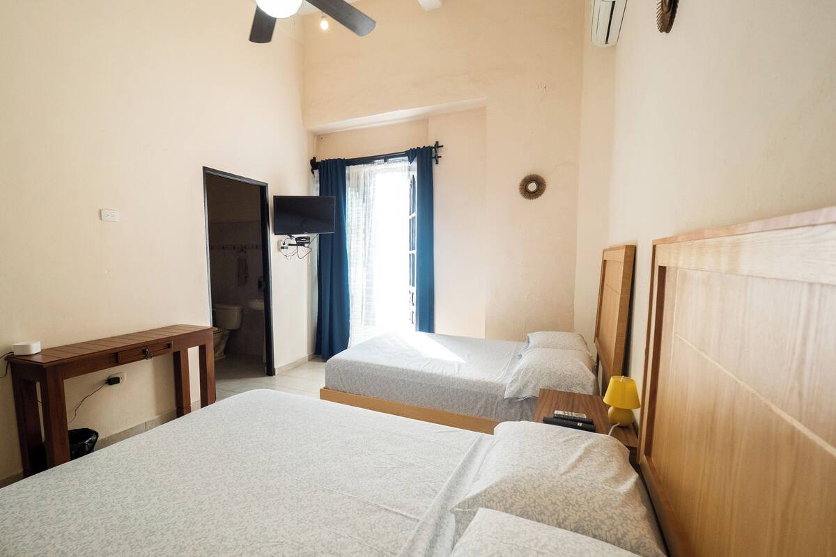 A hotel room with two beds, a ceiling fan, a TV, and a bathroom visible through an open door.