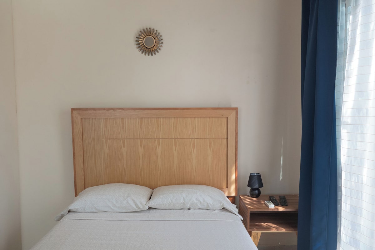 A neatly made bed with a wooden headboard, a bedside table with a lamp, and a wall-mounted light fixture.