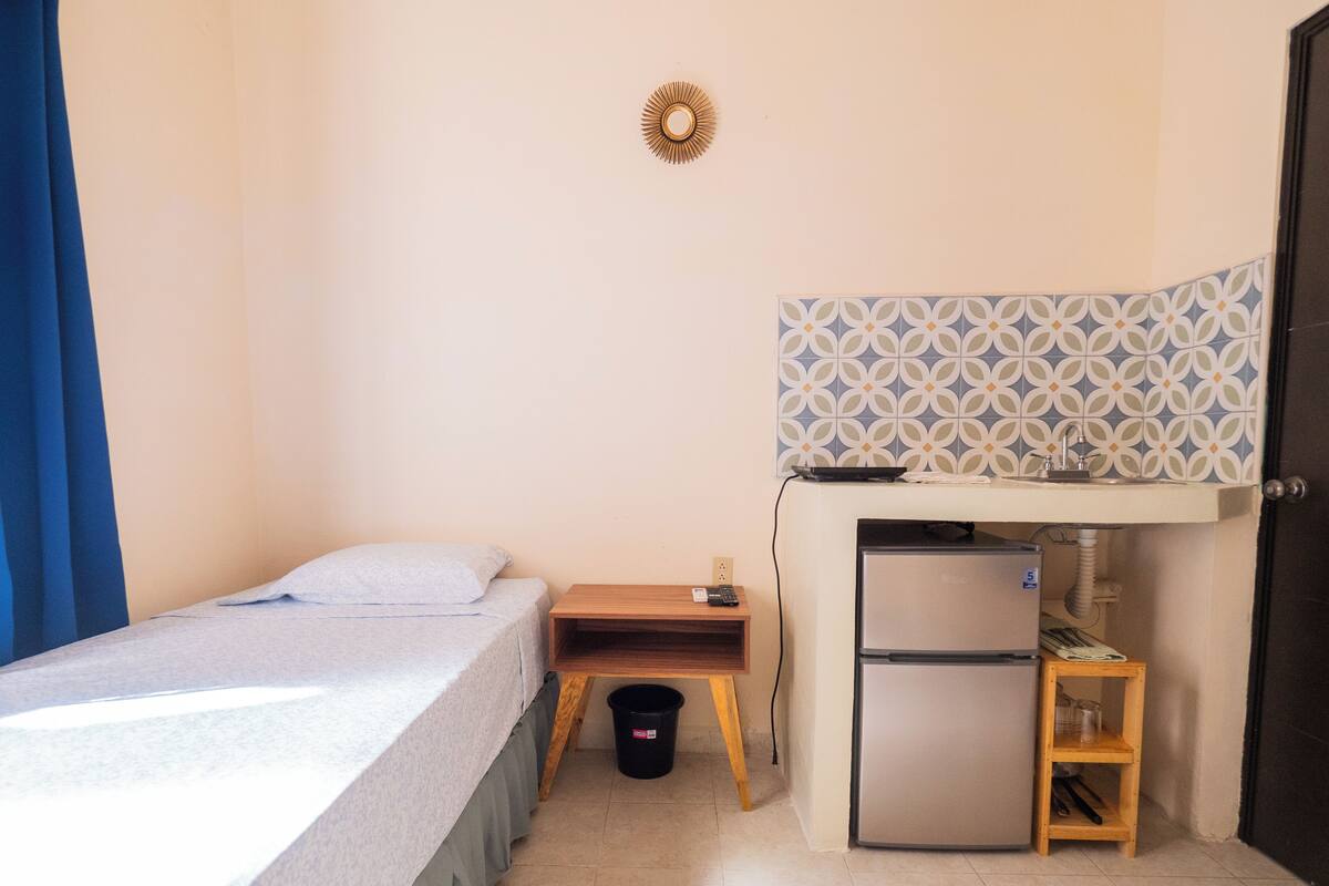A compact room with a bed, a small kitchenette, and a door.