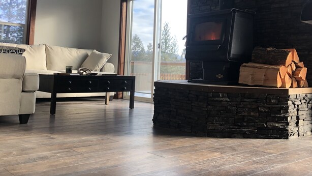 A modern living room with a stone fireplace, a sofa, and a hanging light fixture. - Rocky Mountain Getaway (Plains)