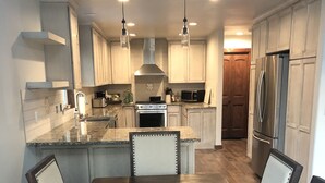 A modern kitchen with a central island, stainless steel appliances, and a dining area with a dark wood table and chairs. - Rocky Mountain Getaway (Plains)